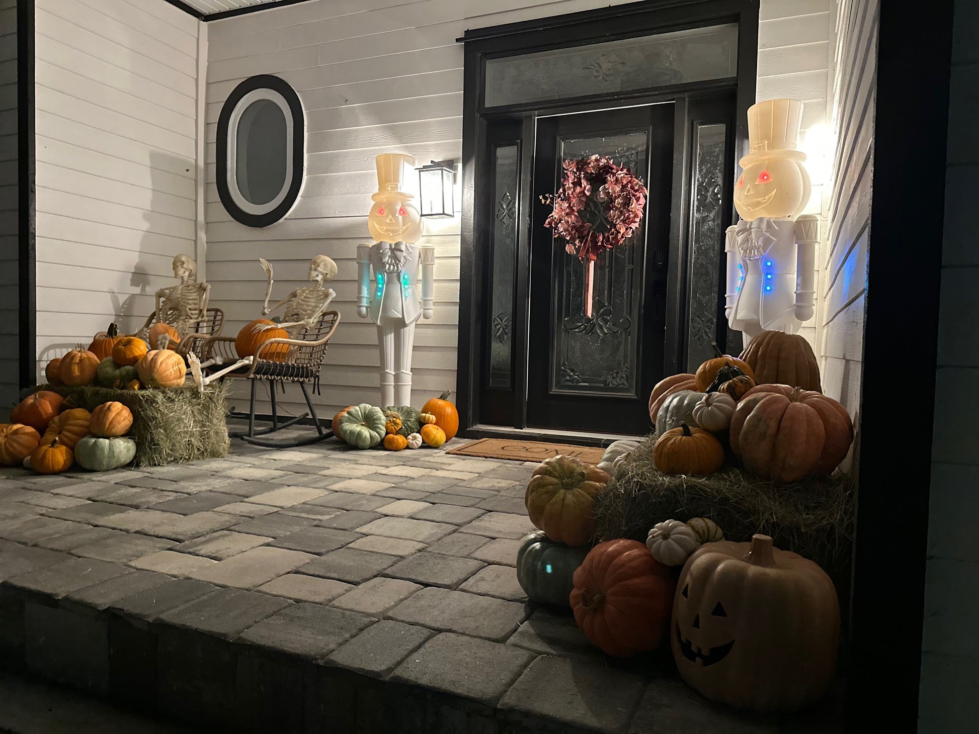Halloween-themed porch with pumpkins, ghosts, and a wreath on a door. Gourgeous Glow pumpkin scape
