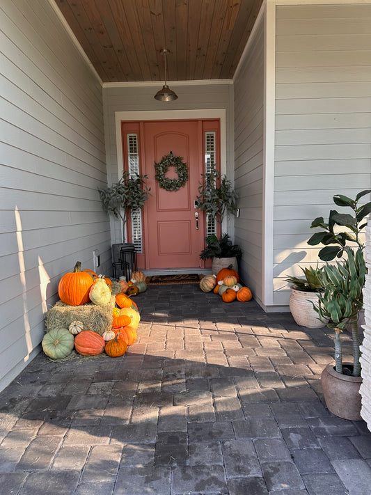 Decorative pumpkins and plants on a stone wall next to a house entrance with a wreath Welcome Home pumpkinscape with hay bale